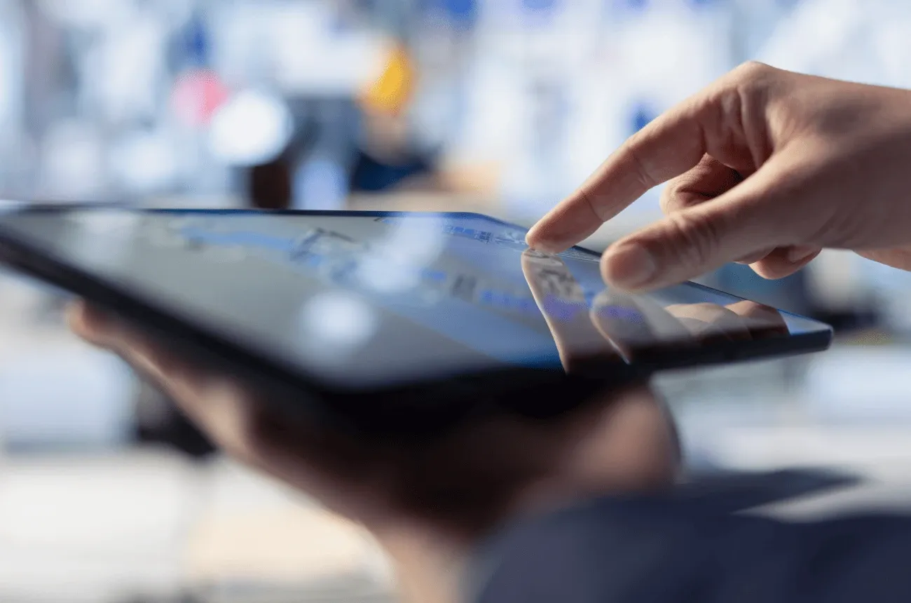 A close-up of a finger tapping the screen of a tablet held in one hand