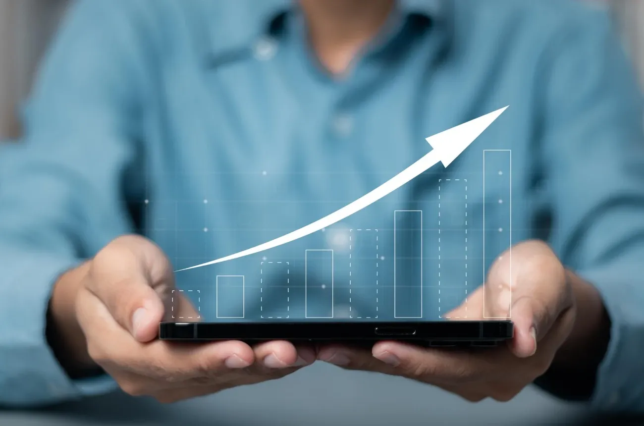 Hands hold a smartphone with a rising bar chart and an upward arrow graphic floating above it