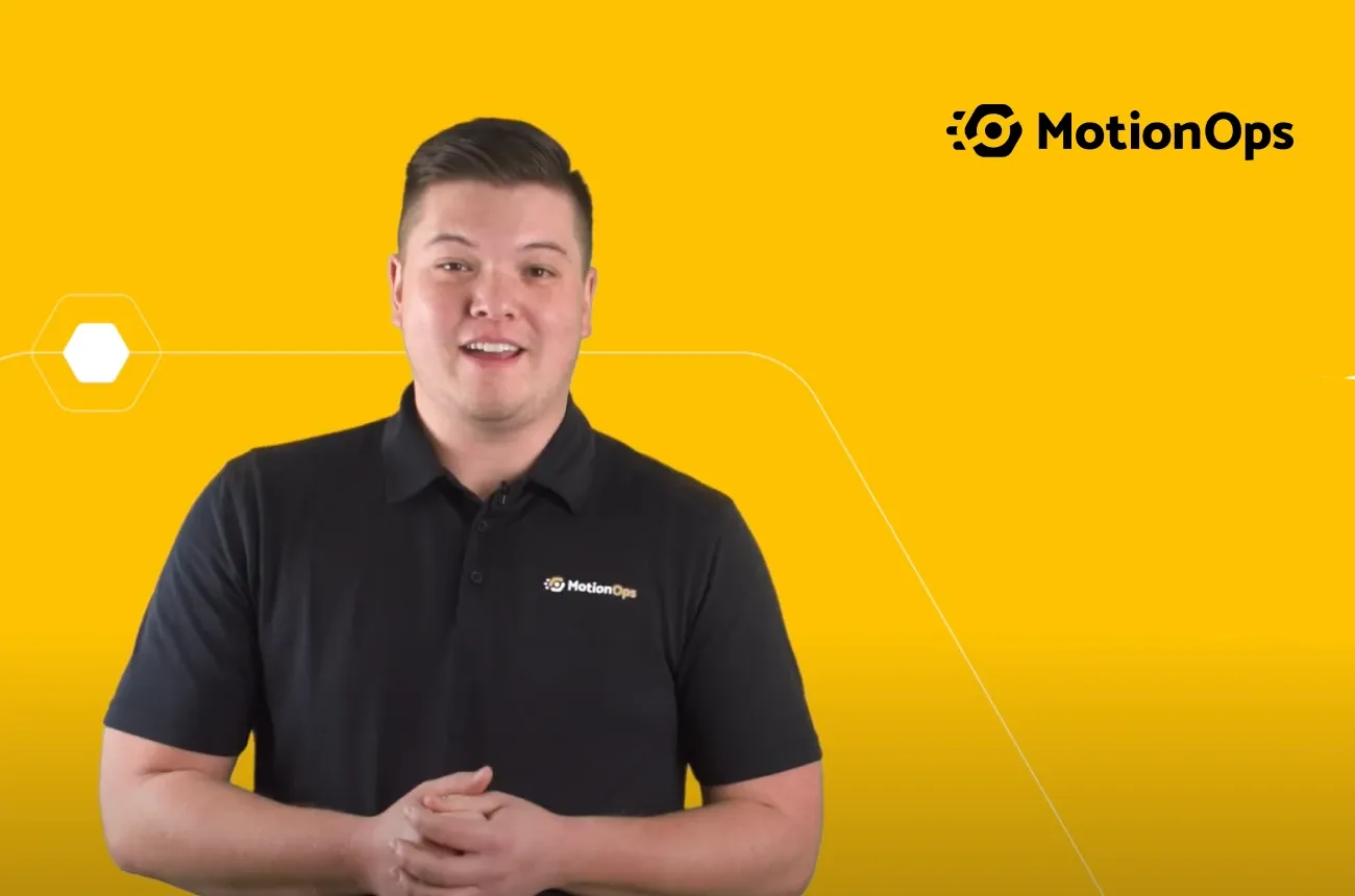 A smiling man in a black MotionOps polo shirt in front of a yellow background with the MotionOps logo