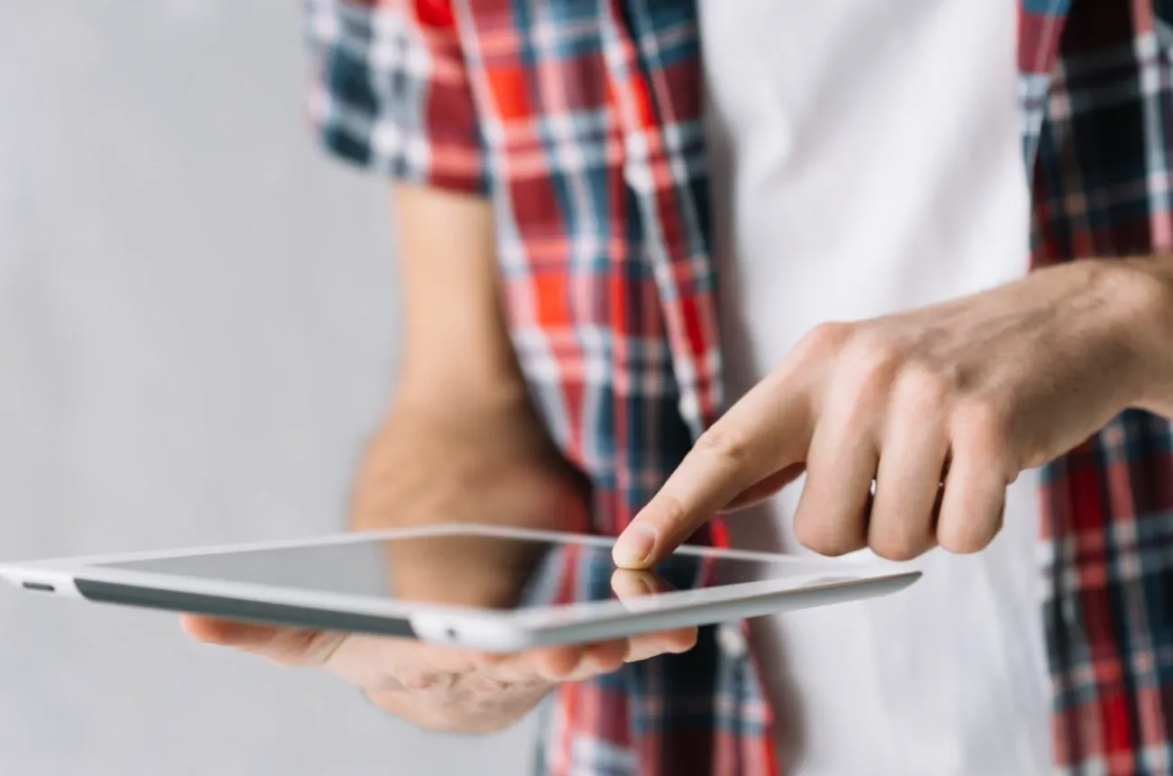 A person in a red plaid shirt tapping the screen of a white tablet
