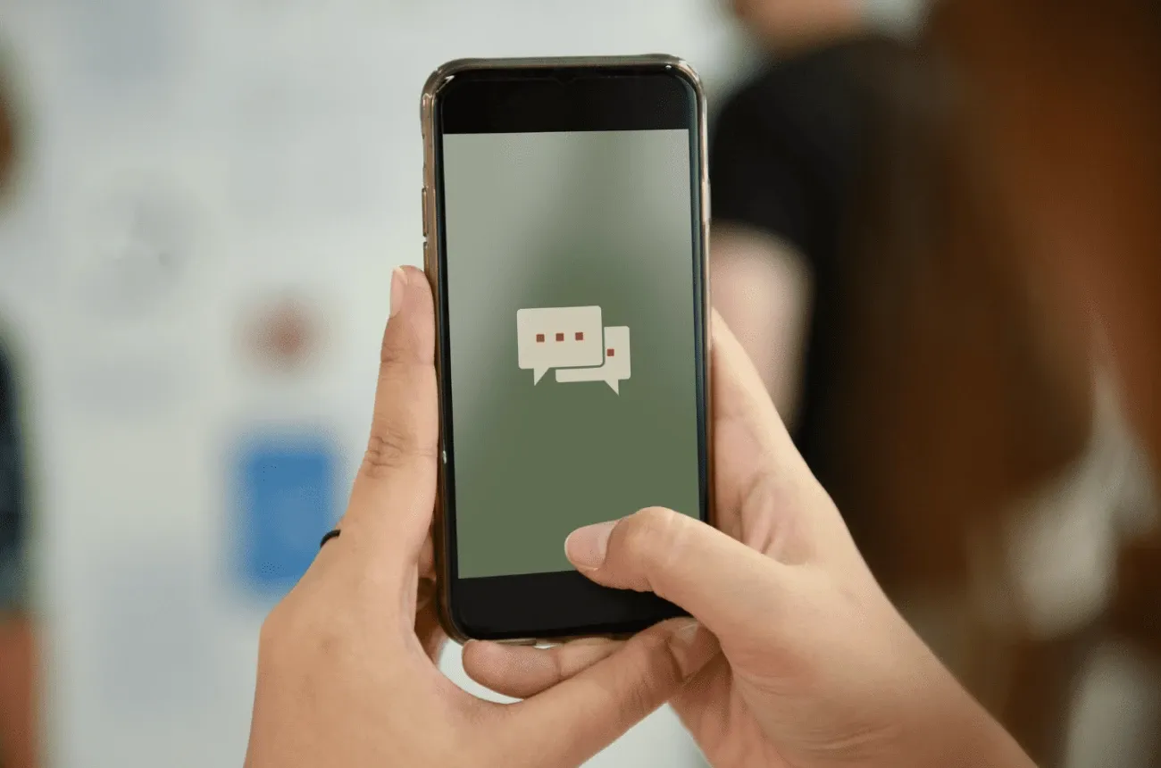 Two hands hold a smartphone showing a chat bubble icon on a green screen