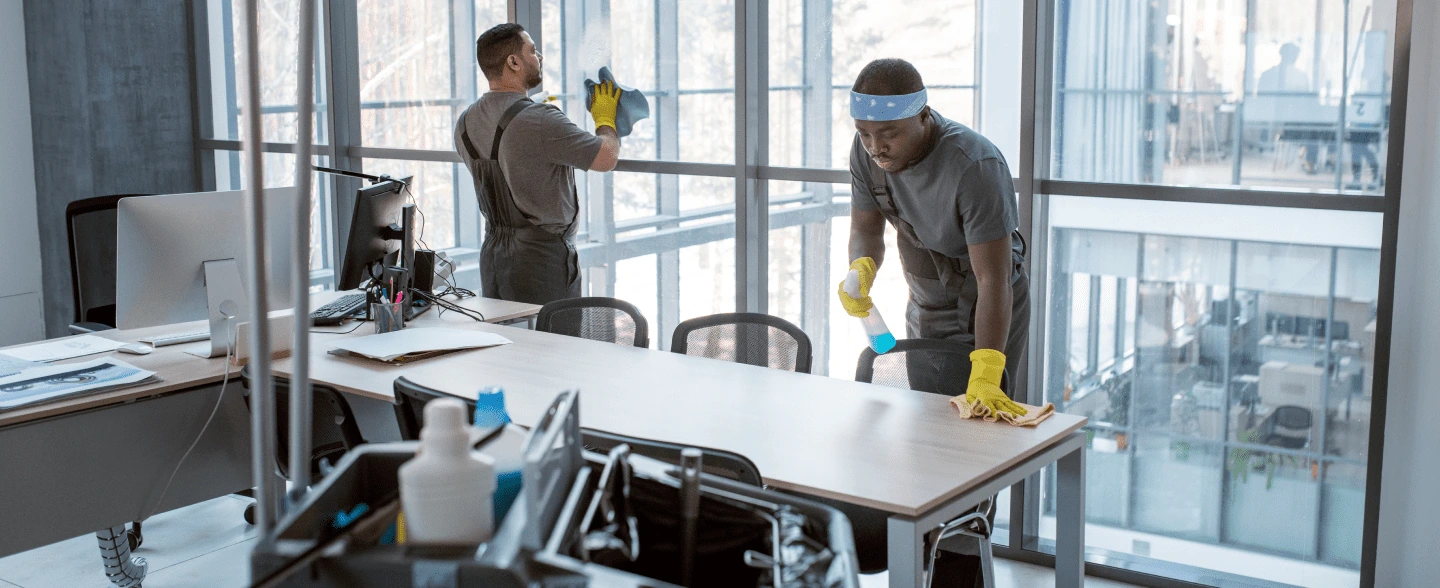 2 cleaners cleaning an office desk and windows
